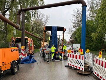 Arbeiter und Absperrungen um Maschinen bei der Reparatur einer Rohrleitungsquerung auf nasser Straße.