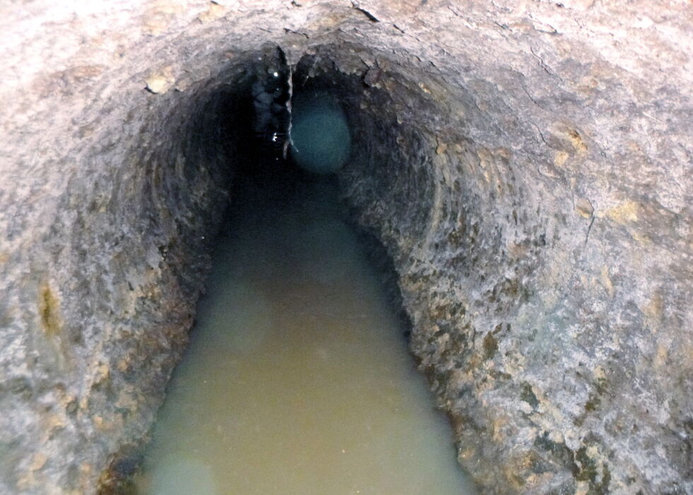 A narrow rocky tunnel filled with shallow muddy water.