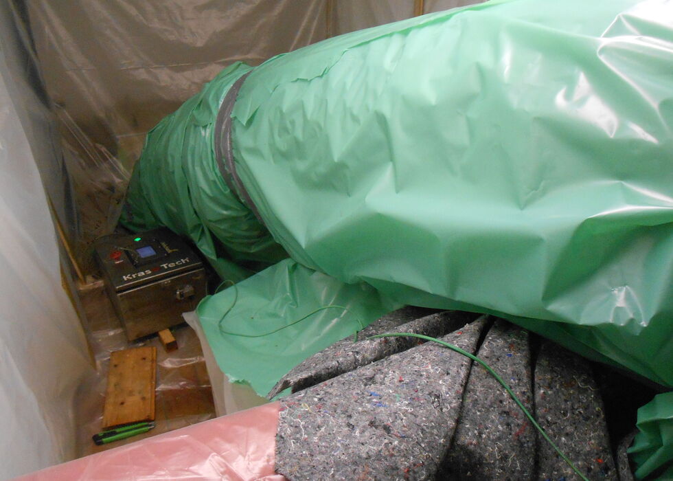 Industrial equipment wrapped in green plastic sheeting inside a work area.