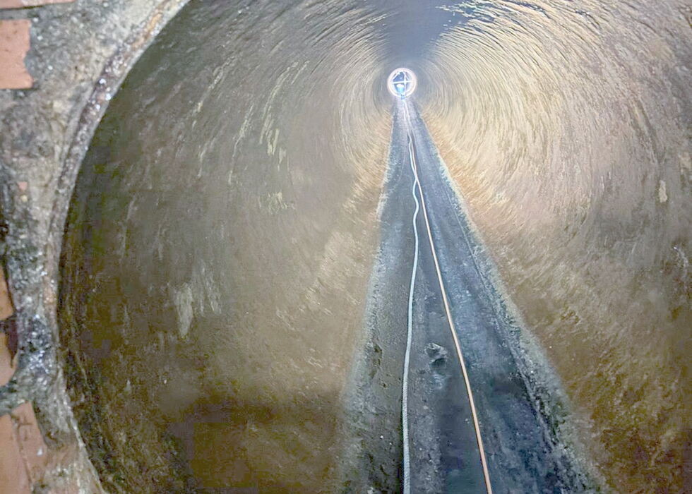 View from inside a circular fountain basin looking up at a central water jet and wet stone walls.