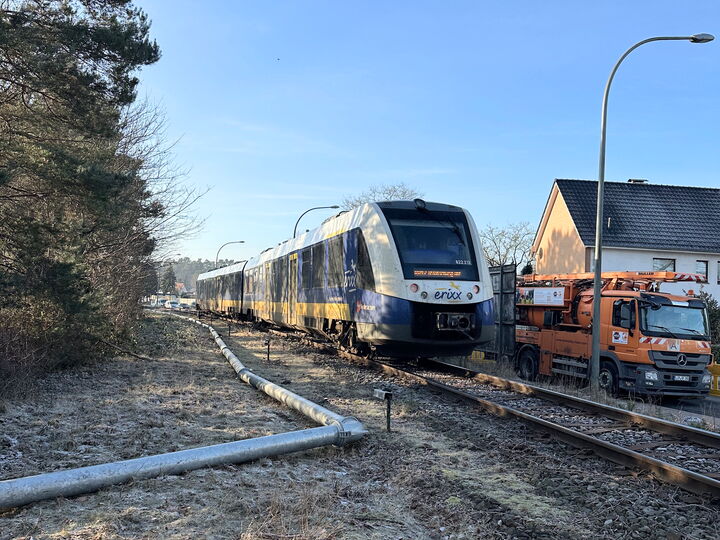 A modern passenger train travels along frosty railway tracks beside houses and maintenance vehicles.