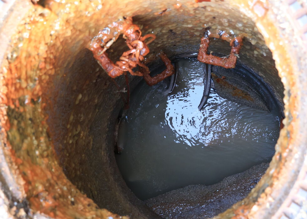Close-up inside a rusty drain pipe showing standing water with dirt and debris.