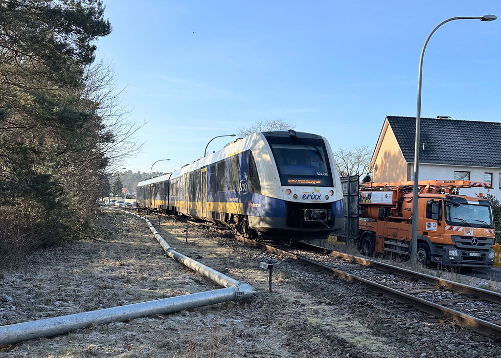 A modern passenger train travels along frosty railway tracks beside houses and maintenance vehicles.