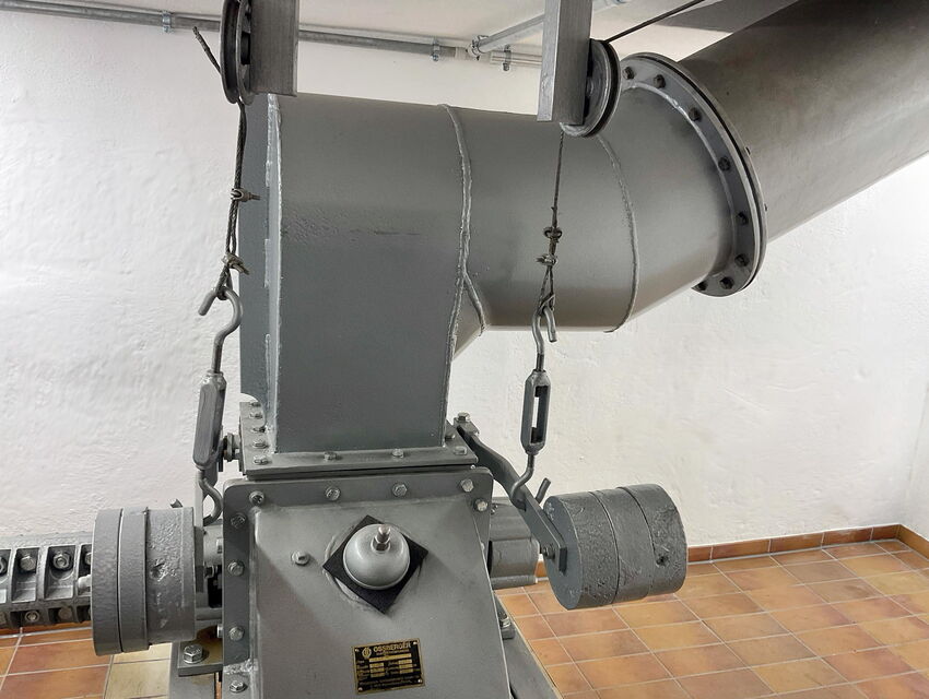 Close-up of a gray industrial machine connected to large ventilation ducts in a tiled room.