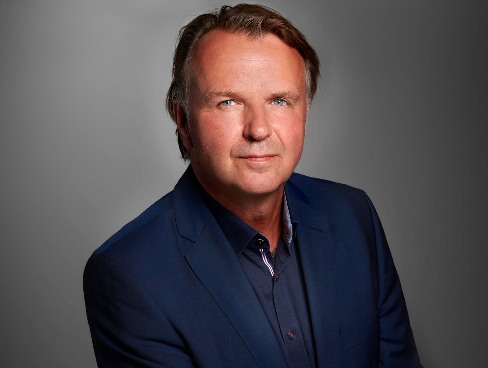 Studio portrait of a middle-aged man in a navy blazer against a gray background.