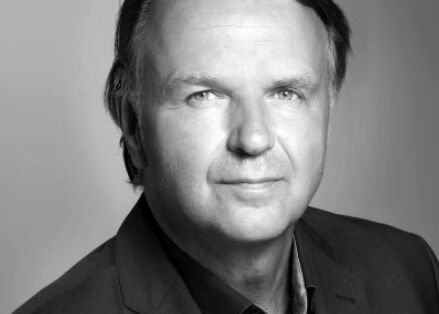 A black and white professional portrait of a man in a suit, showing a confident expression.