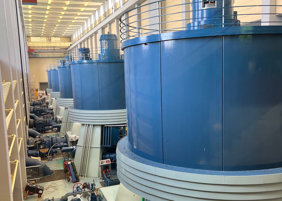 Interior of a power plant with rows of large blue generators and machinery.