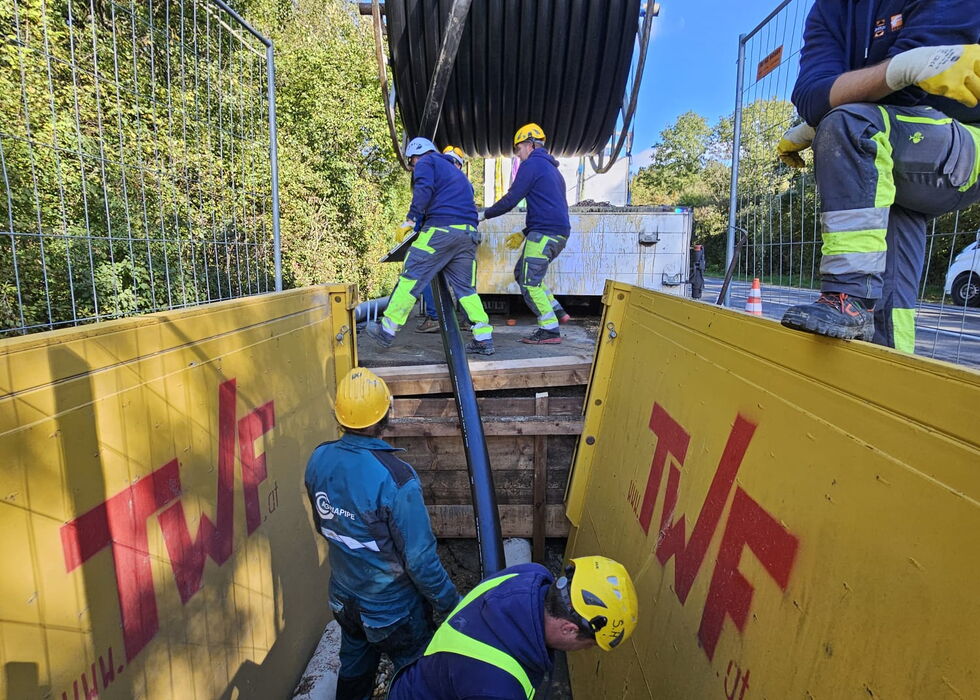 Bauarbeiter in Schutzkleidung transportieren und sichern einen großen Leistungstransformator auf einer Arbeitsplattform im Freien.
