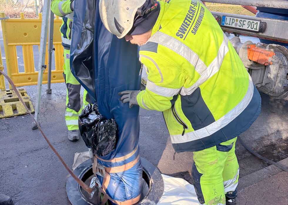 Worker in high-visibility gear seals a manhole with a blue liner during sewer inspection work.