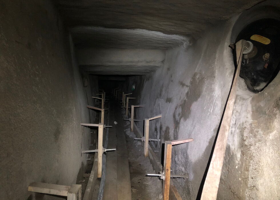 Dark underground tunnel with wooden structural supports and a pipe along the floor