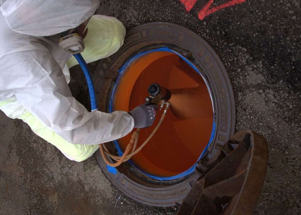 A technician in protective clothing examines an orange pipe opening inside industrial equipment.
