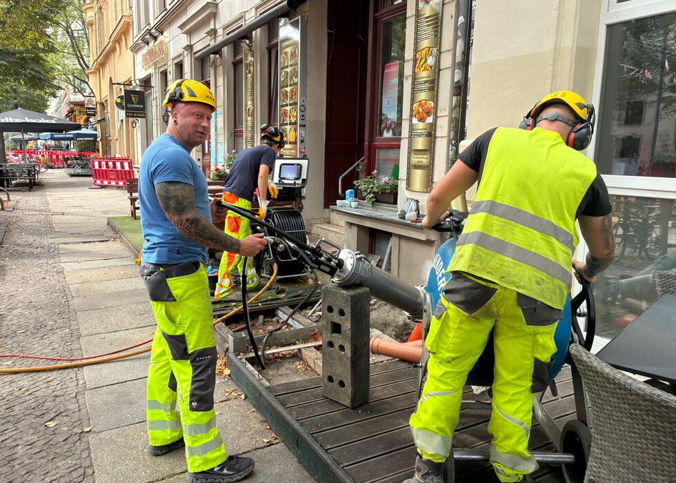 Zwei Straßenarbeiter in Warnkleidung schneiden mit einer Betonsäge den Gehweg in der Stadt.