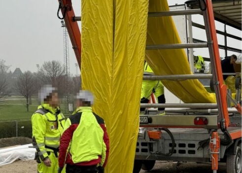 Arbeiter in Sicherheitskleidung entladen ein großes gelbes Material von einer Maschine auf einer Baustelle.