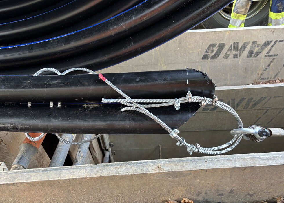 Ein Arbeiter befestigt Seile und Kabel an einer Rohrleitung auf einer Baustelle.