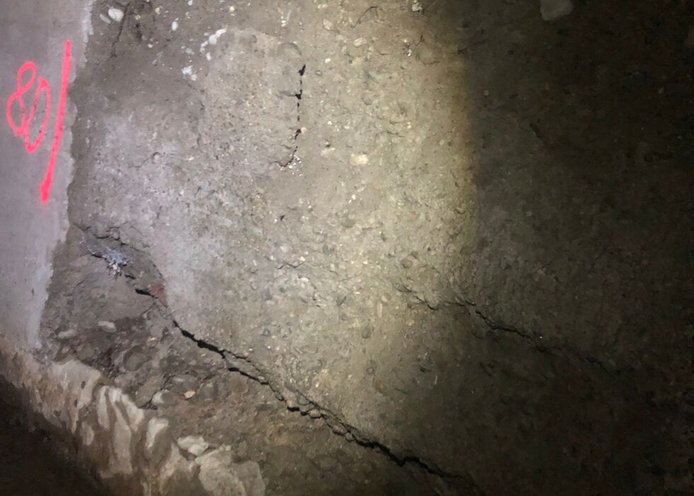 Close-up of a cracked concrete floor with visible damage and debris in dim light