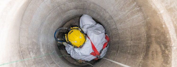 A technician in protective gear descends into a deep tunnel, using safety harnesses and equipment for secure access.