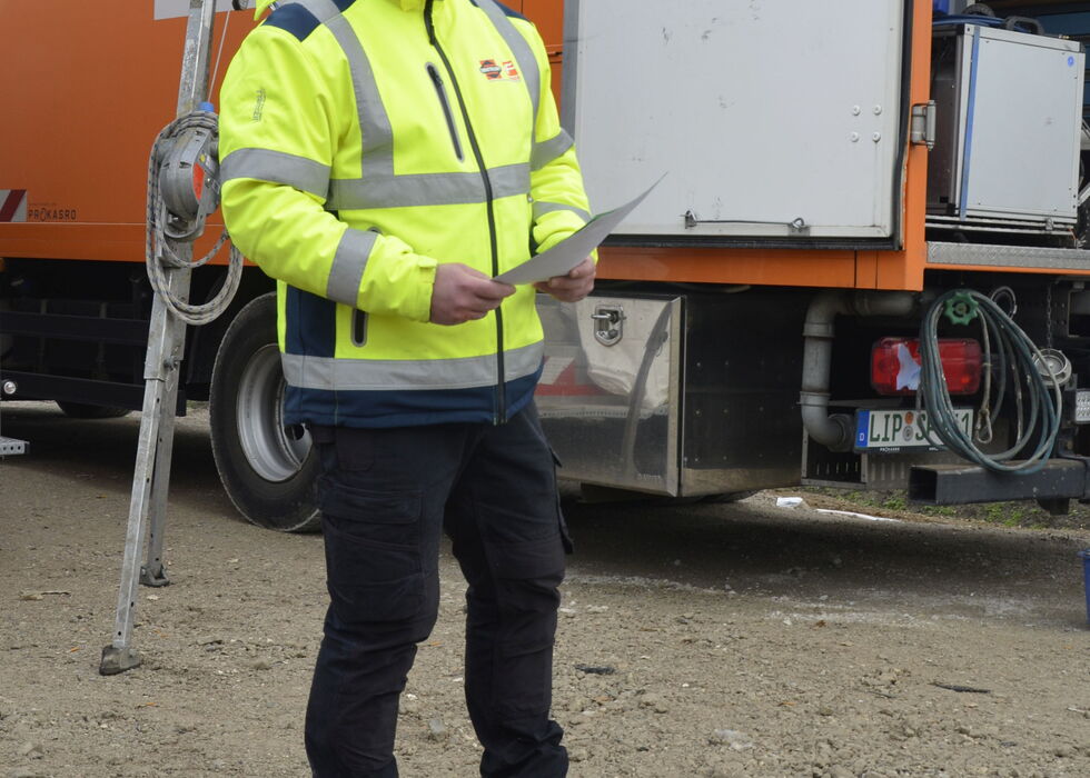 Ein Arbeiter in Warnjacke liest Notizen neben einem Servicewagen auf einer Baustelle.