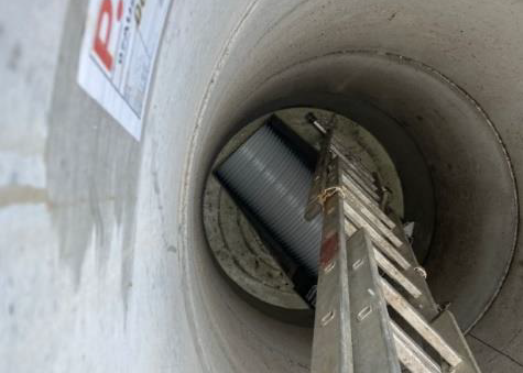 View down a concrete pipe with a ladder leading to a worker or equipment below.