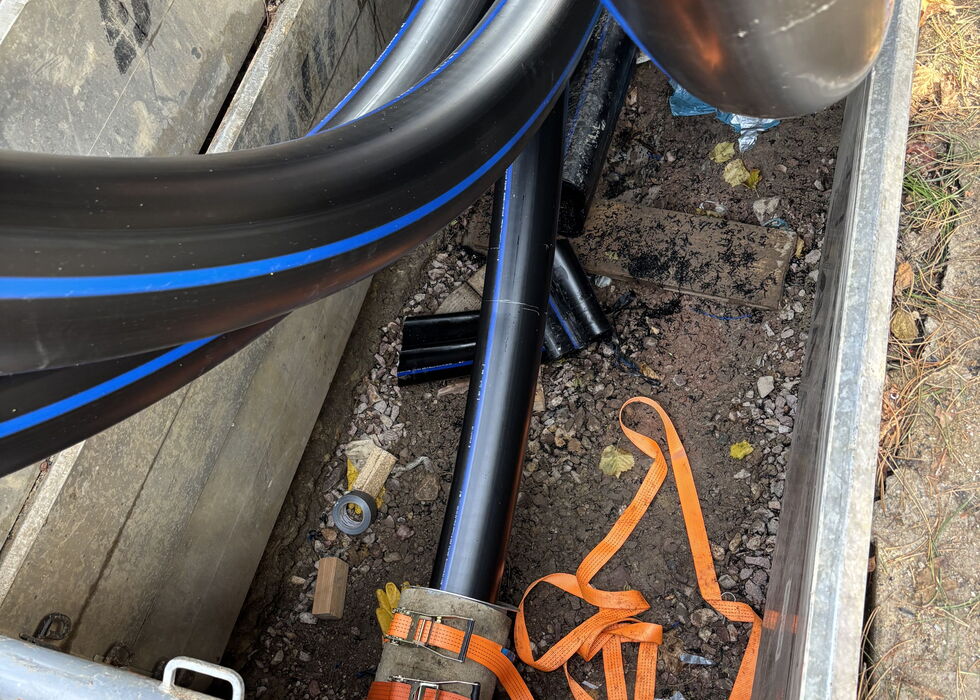 Blaues und orangefarbenes Kabel in einer Betondurchführung neben einem Metallrohr und Baustellenresten.