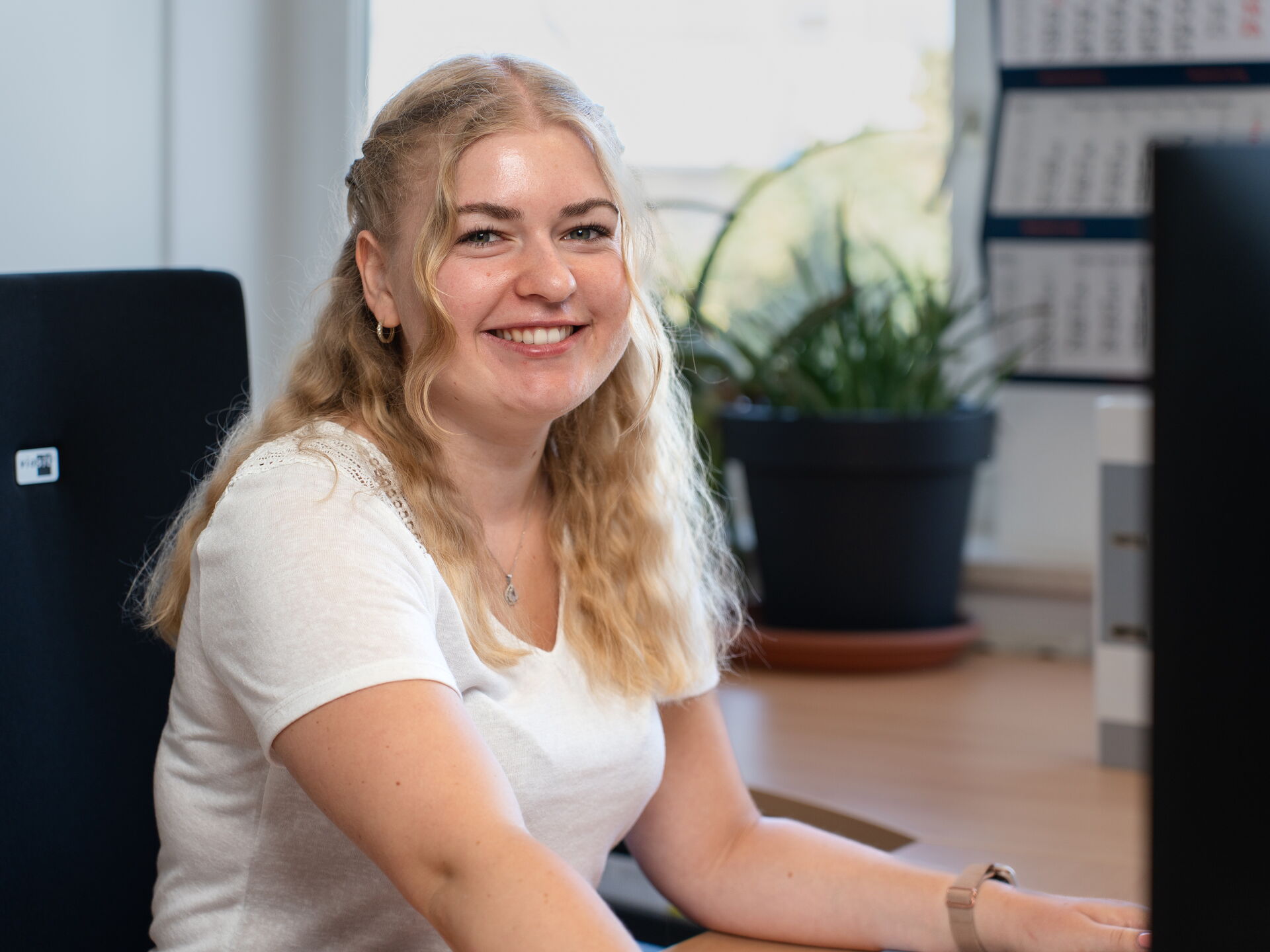 Young woman with blond hair sitting on office chair and smiling while working at a computer