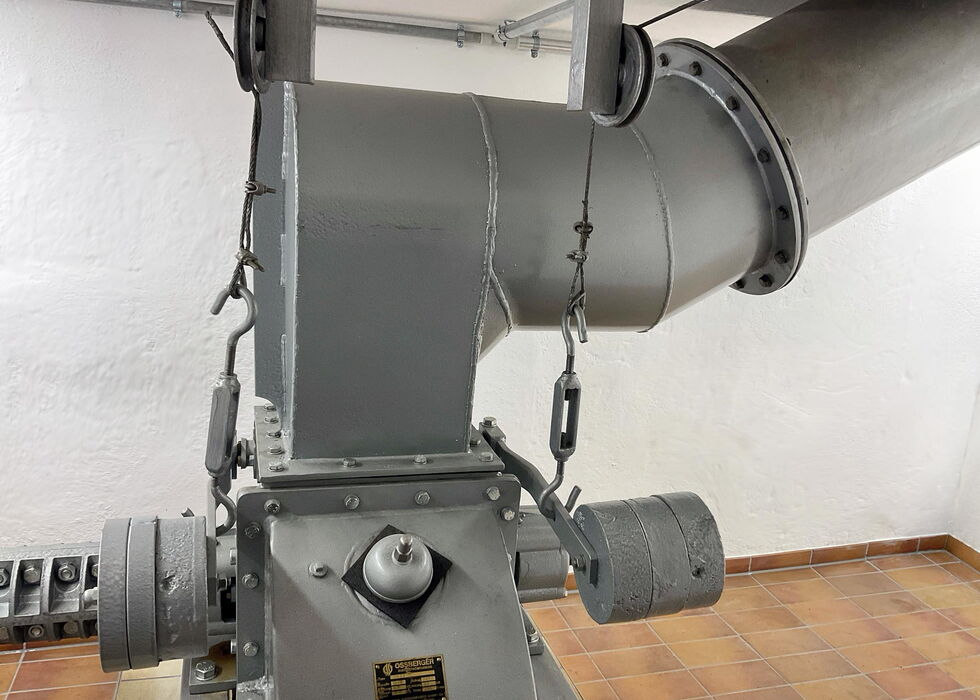 Close-up of a gray industrial machine connected to large ventilation ducts in a tiled room.
