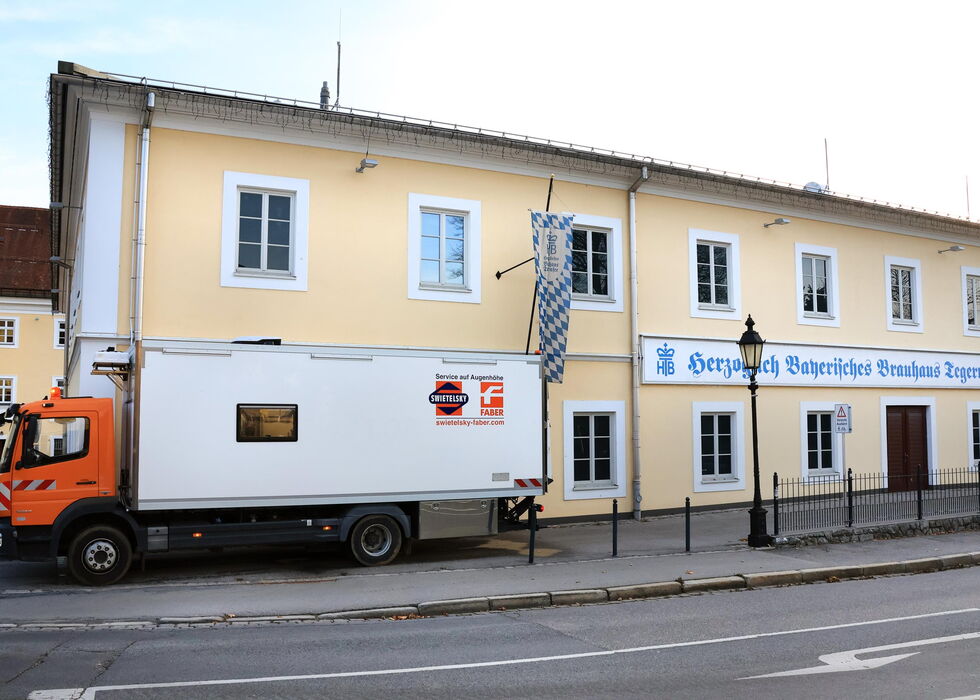 An orange-and-white delivery truck parked beside a yellow building with a sign in German.