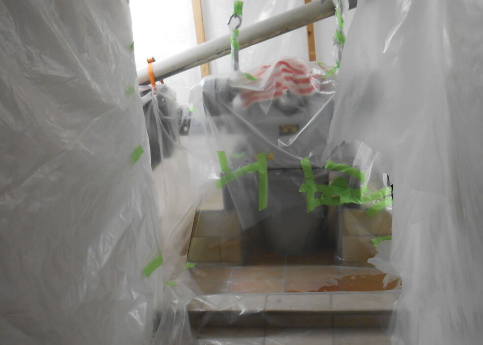 Plastic sheeting covers a doorway and room during renovation, with tools and a pole visible inside.