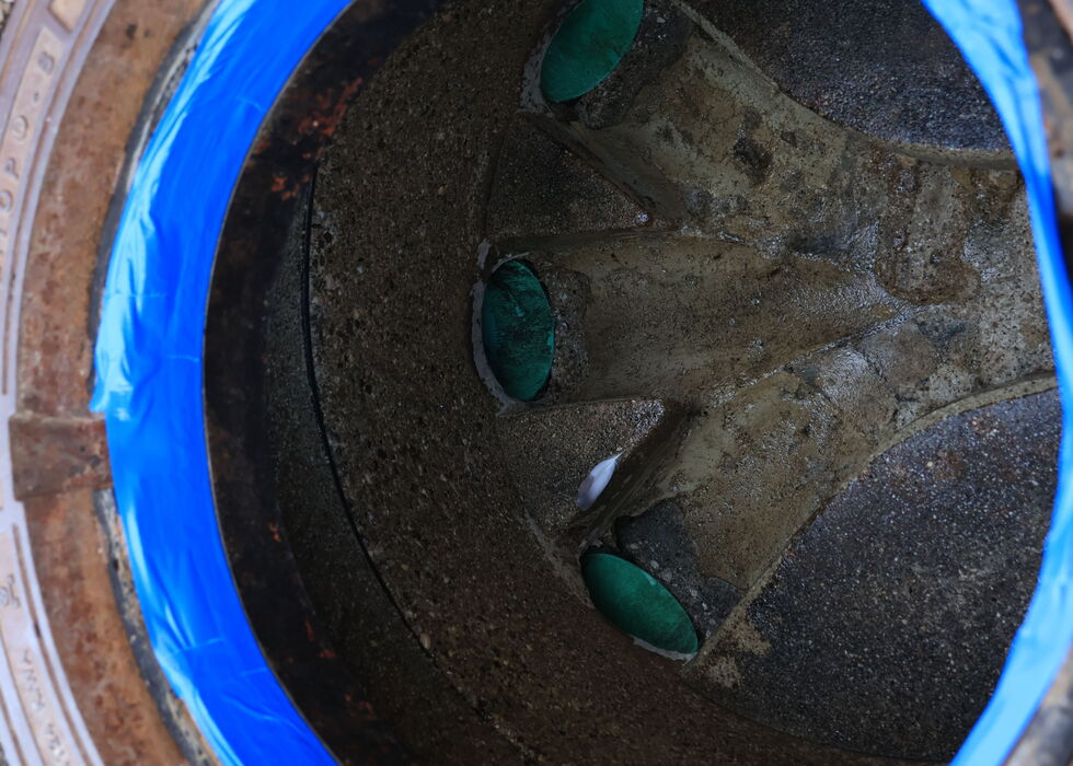 Looking down into a well with a blue rim, stones, and green leaves scattered on the bottom.