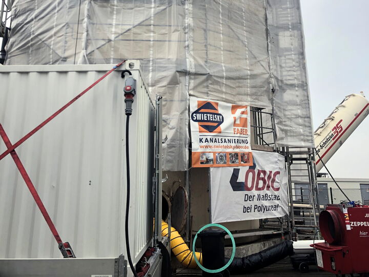 A tall building wrapped in protective plastic and scaffolding at a construction site with equipment in front.
