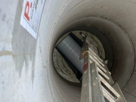 View down a concrete pipe with a ladder leading to a worker or equipment below.