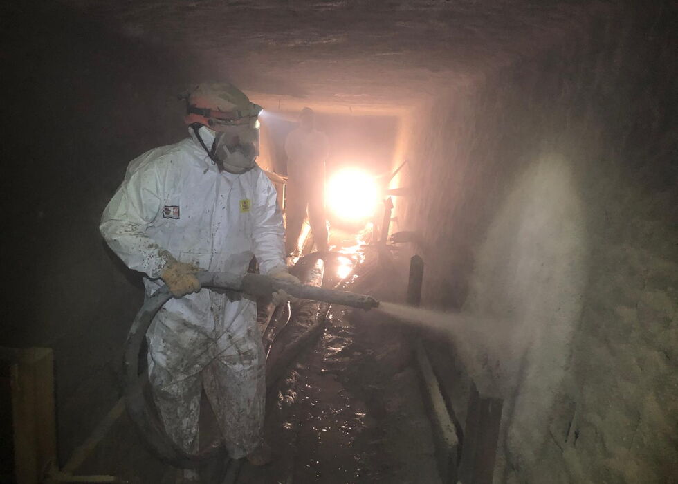 Person in protective gear spraying inside a dimly lit underground tunnel