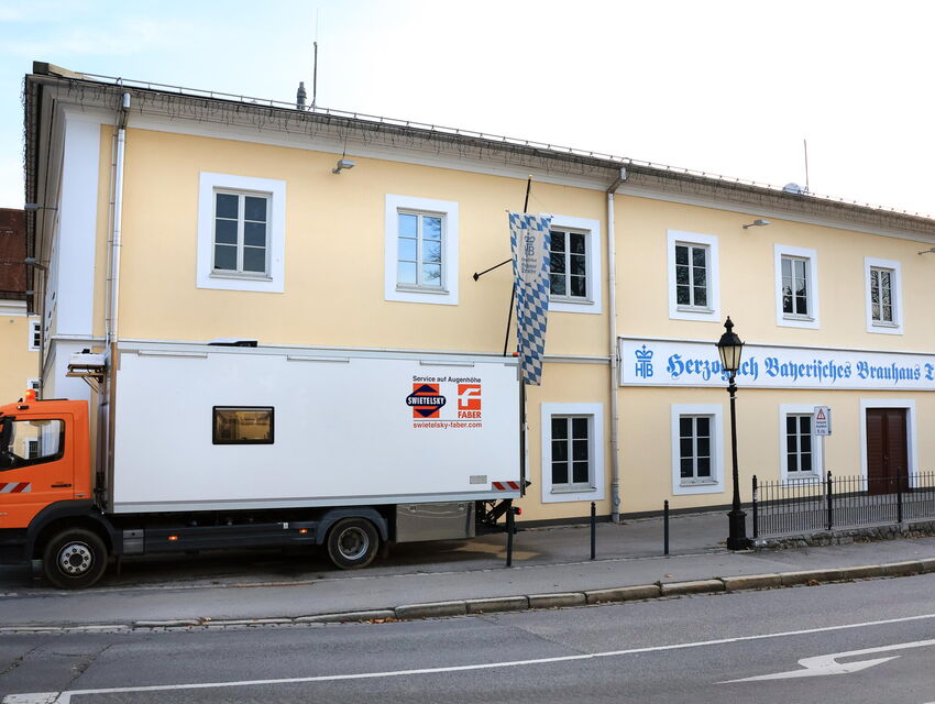 An orange-and-white delivery truck parked beside a yellow building with a sign in German.